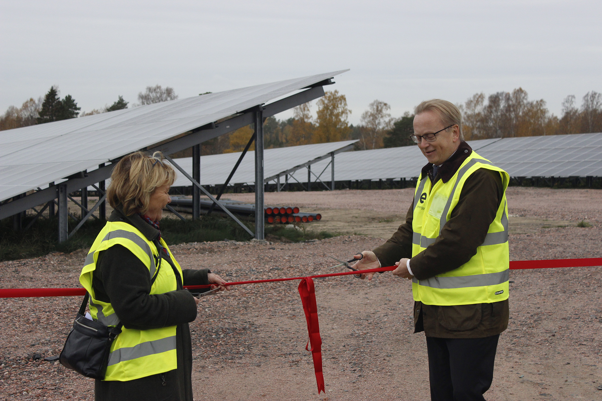 En kvinde og en mand i gule veste klipper en rød snor foran en solcellepark